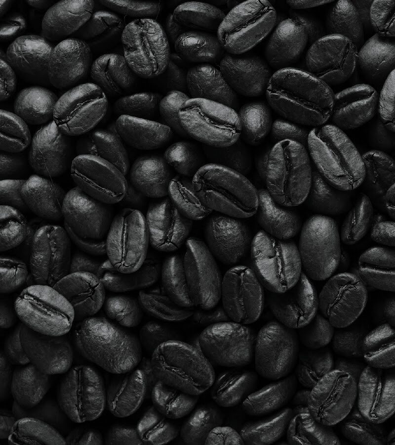 The Two Mugs logo, two smiling cartoon mugs, in white over a field of dark roasted coffee beans